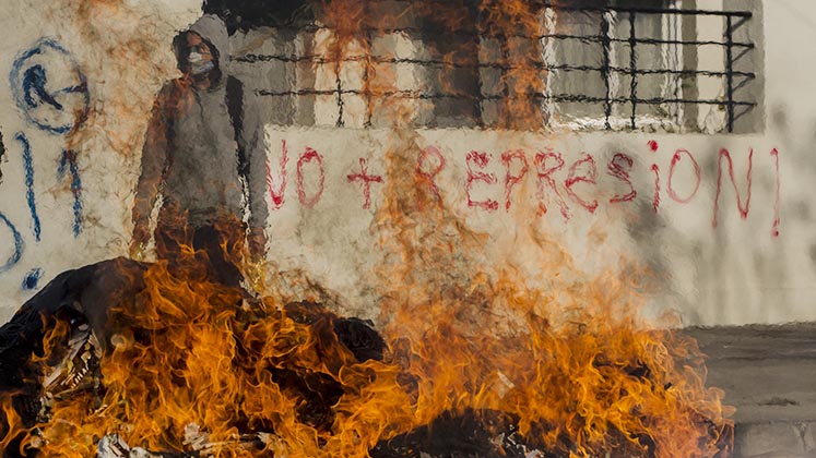 A masked Chilean protester stands behind a burning barricade in front of graffiti that reads 'no more repression'