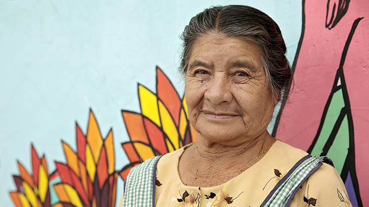 A Guatemalan woman stands in front of a mural signifying women’s empowerment and freedom from violence that was painted by women leaders and community members