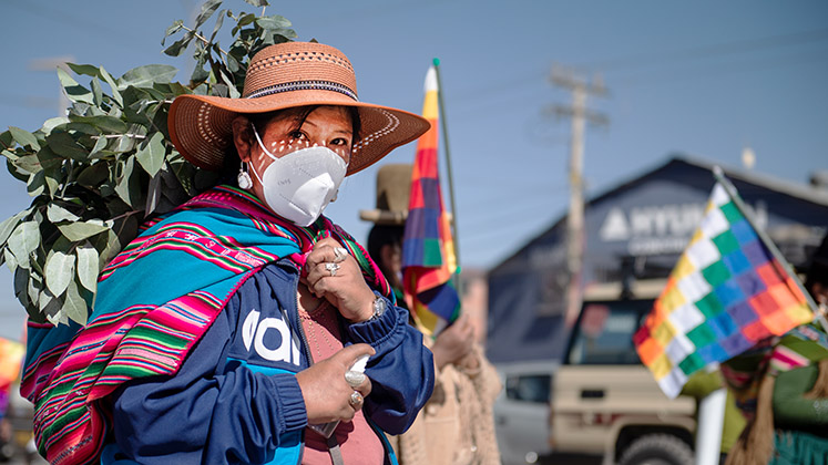 An indigenous woman in a face mask in Bolivia looks into the camera as she takes part in a political rally in El Alto