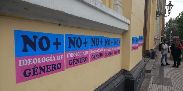 Outside wall of a building with a row of poster stickers in blue and pink that read No + ideología de género in all capital letters