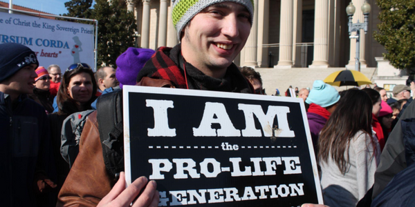 Photograph of protester holding a sign that reads "I am the pro-life generation"