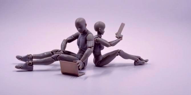 Two robots, sitting, using laptops