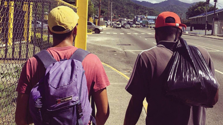 Two men with backpacks walking up the side of a road