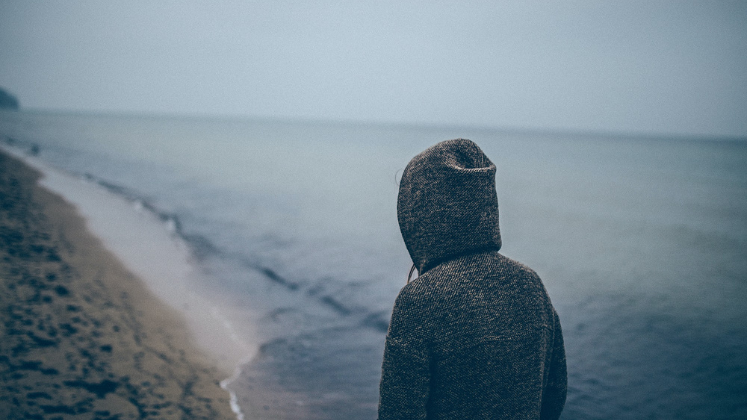 Person in hoodie looking out at sea