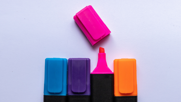 A blue, a purple, an pink and an orange highlighter in a row, with the lid off the tip of the pink highlighter