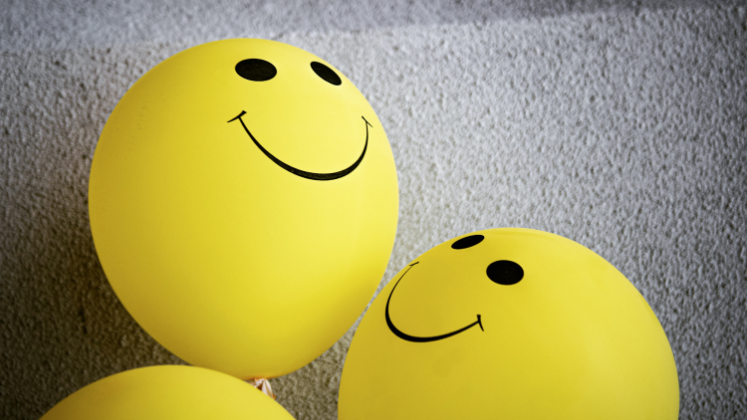 Two balloons with smiley faces on them against a grey background