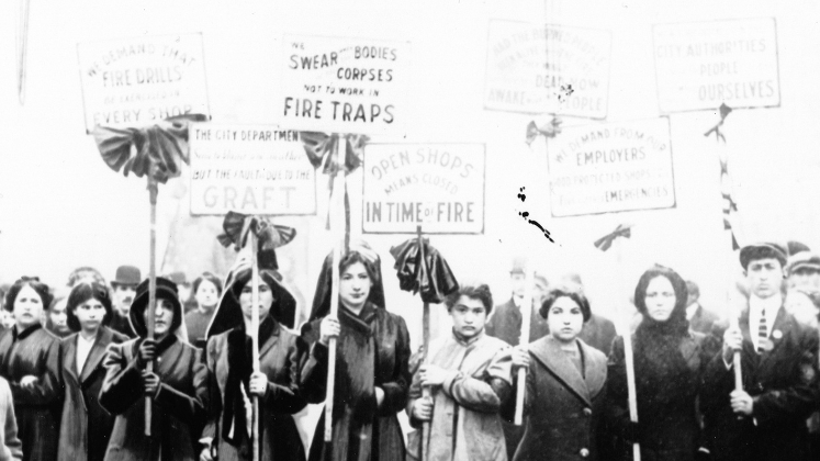 Mourners picket after the Triangle fire. Their signs, hung with black crepe, accuse shop owners of graft, locked doors, and managing workers in fire trap