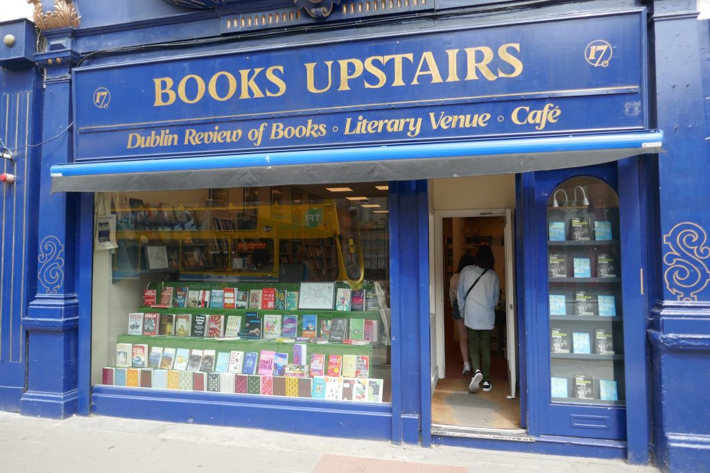 Image of the blue shopfront of Books Upstairs, Dublin, showing a person entering and colourful books in the window.