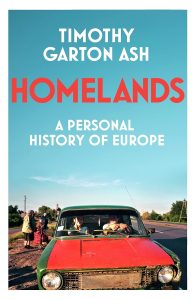 Cover of Homelands by Timothy Garton Ash showing a man and woman in a red and green car on the side of the road with elderly people and a blue sky and trees in the background.