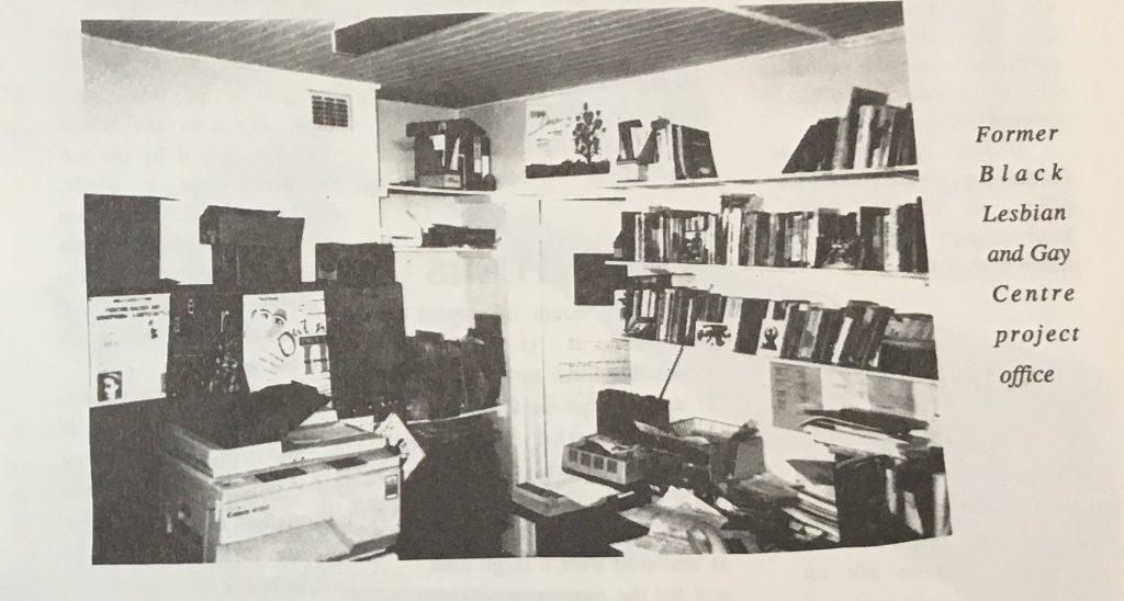 A photo from a newsletter of an office. It includes shelves with books, a printer/copier machine and other generic office equipment.. 