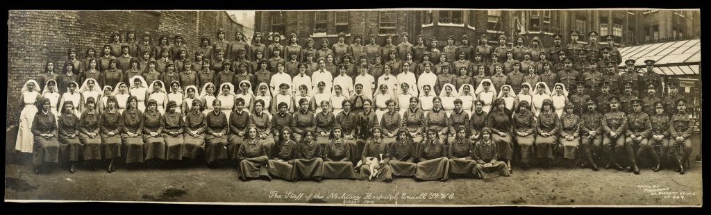 The Staff of the Military Hospital Endell St, August 1916. Drs Flora Murray and Louisa Garrett Anderson seated on chairs centre, Anderson with dog, eleven doctors each side of them (no veils, dark lapels); Matron Grace Hale centre behind; Quartermaster Olga Campbell in front row with dog; orderly Nina Last, sixth from left on the top row; nurse Barbara Last, third row down, second from left of the women dressed in white. The last woman on the right hand side without a veil is believed to be Eleanor Elizabeth Bourne, an Australian doctor. LSE