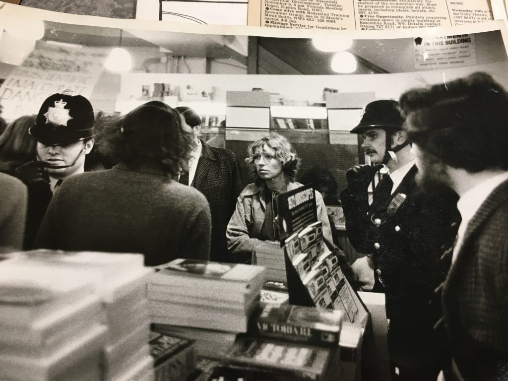 A bookshop scene with stacked titles. Also a protestor in the centre of the photo surrounded by police.
