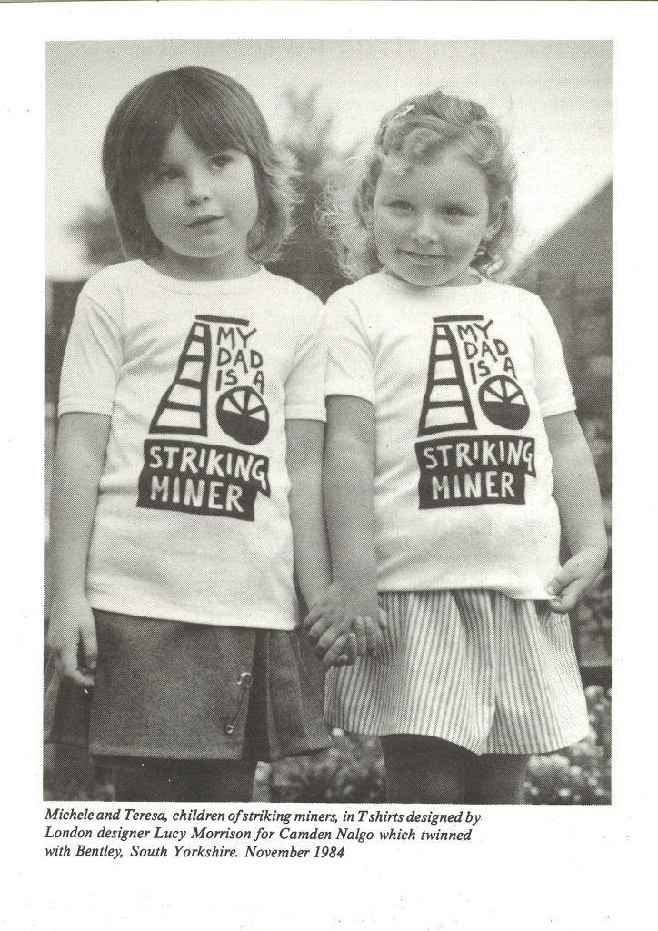 A page from a book with a photo of two children of striking miners wearing T-shirts with "My Dad is a Striking Miner" written on them. 