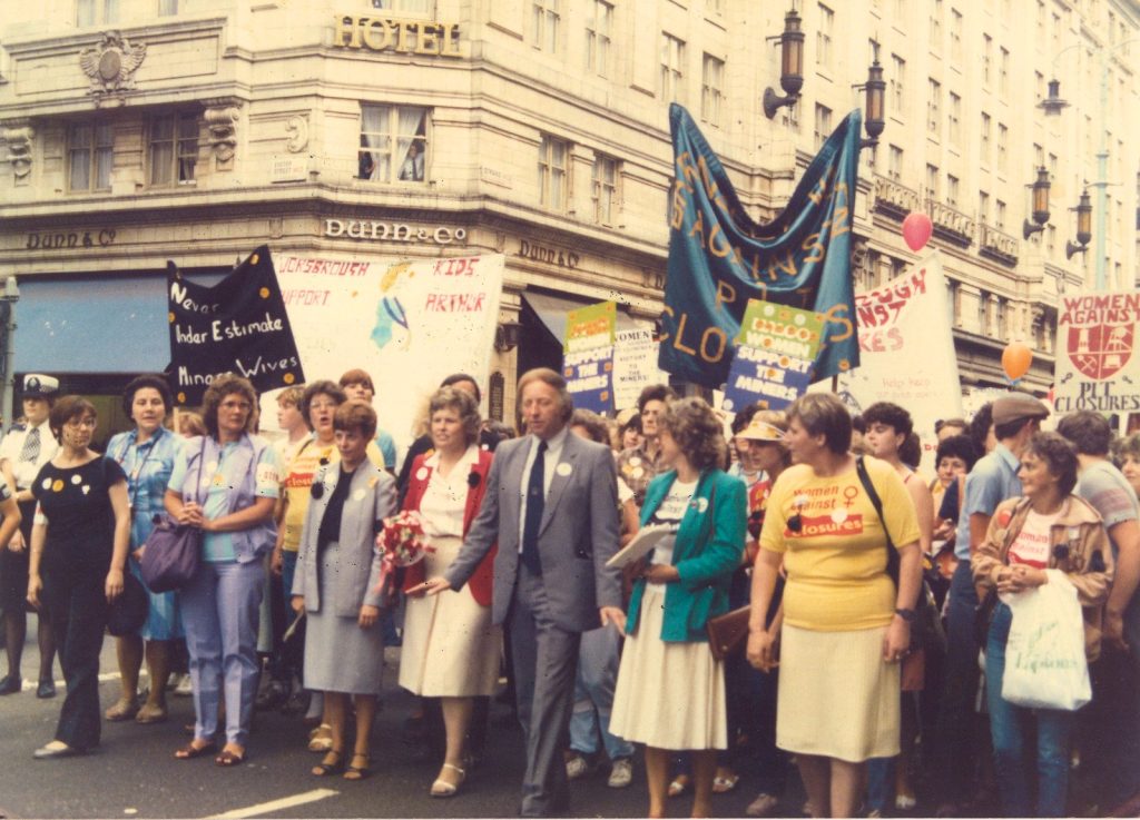 A large group of people including Jean McCrindle and Arthur Scargill leading a march down the Strand in London. There are various banners on show, including ones (and T-Shirts) from the 'Women Against Pit Closures' campaign. 