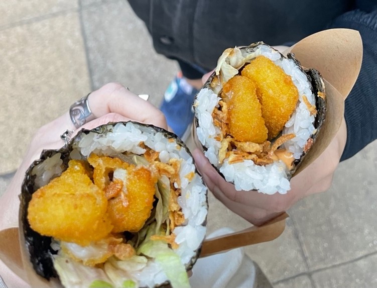 two hands holding a large Japanese street food roll with sushi rice and crispy crumbed filling from the restaurant Crispy Rolls