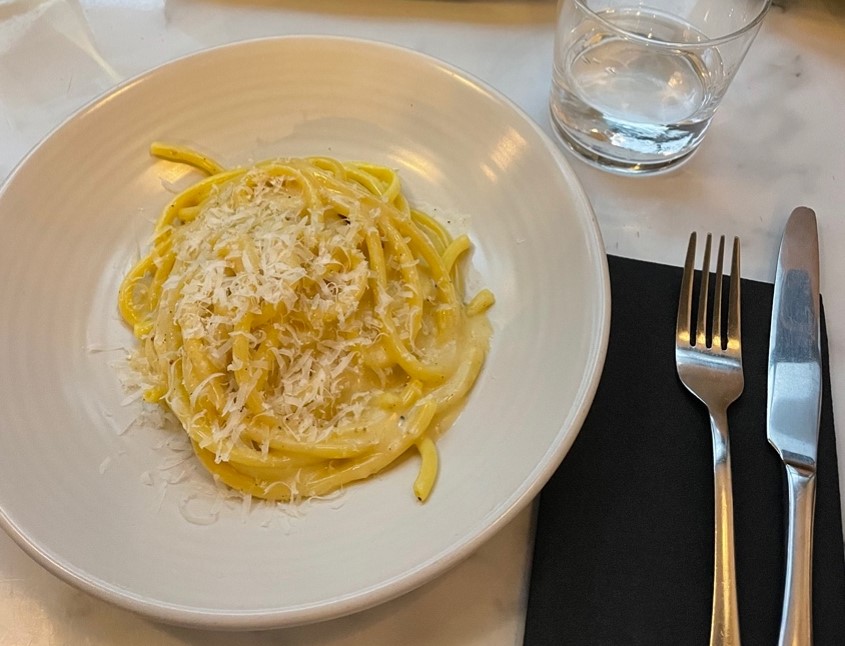 white plate filled with pasta on a table setting with fork and water at the restaurant Bancone