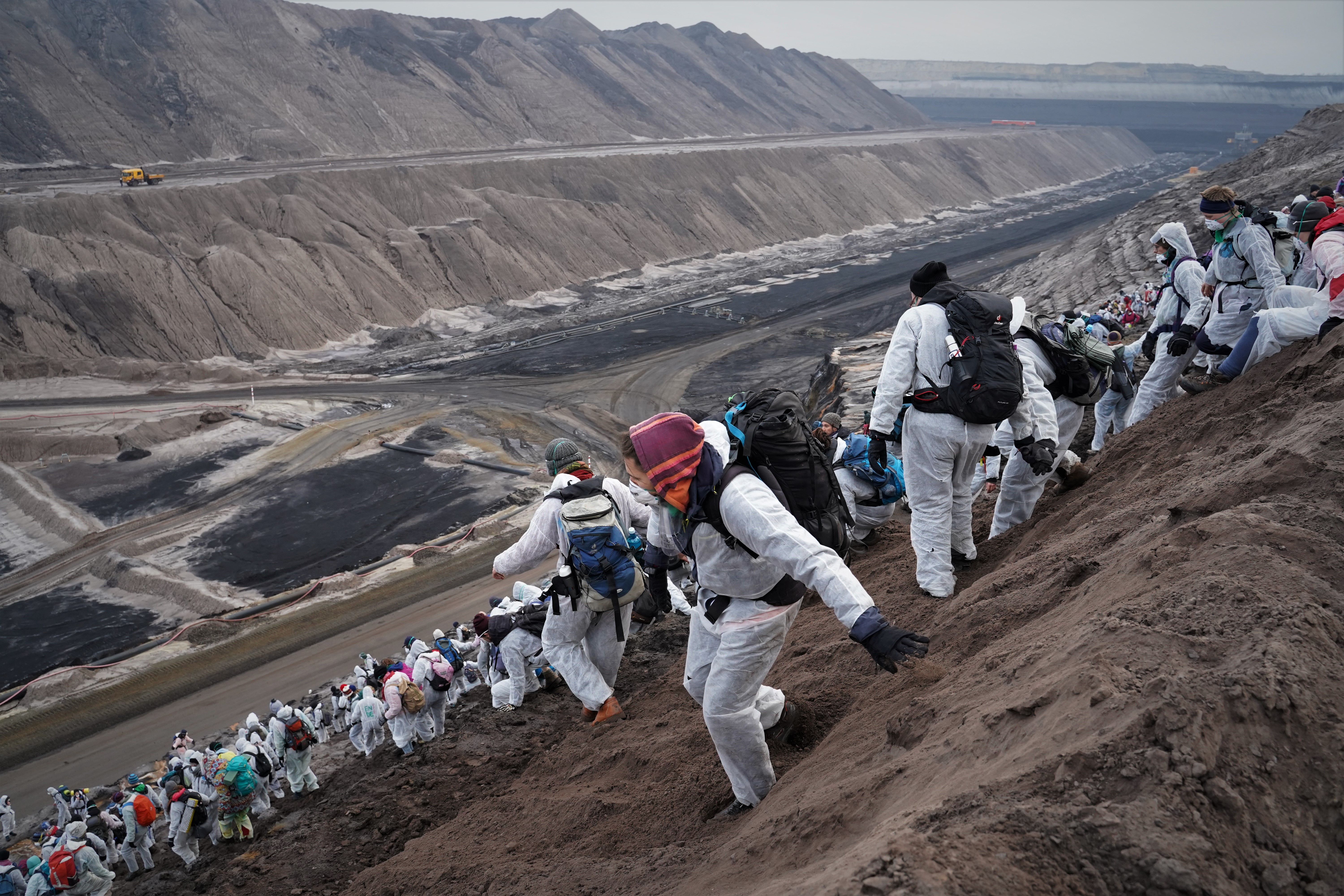 A lignite opencast mine in the German part of the region of Lusatia next to the Polish border. Protestors in white hazmat suits descend the steep edges of the mine.