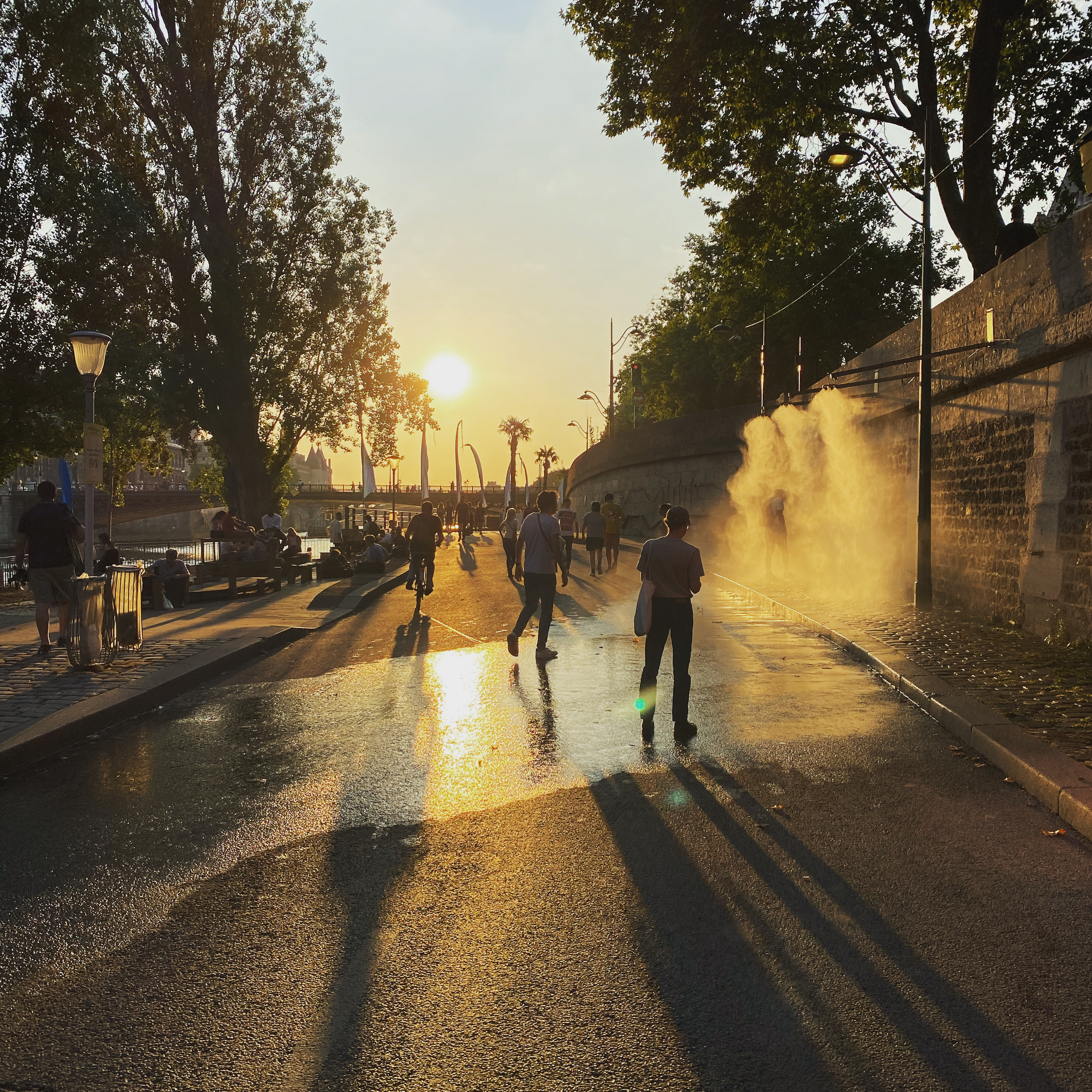 People walking and cycling on a pedestrianised street in Paris. The heat of the day can be seen from the water evaporating on the street.