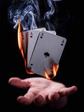 Deck of cards with smoke and flames hovering above a hand